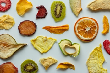 A collection of various dried fruit slices spread out on a white surface, including oranges, kiwis, peaches, pears, and strawberries. The arrangement showcases diverse shapes, textures, and vibrant colors.