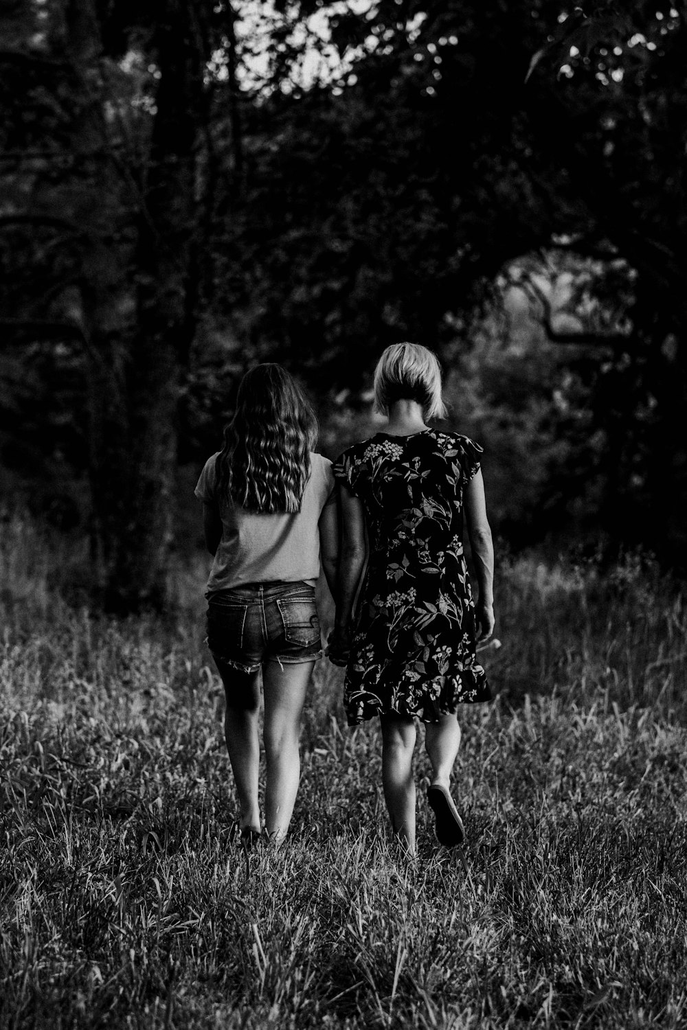 grayscale photo of 2 women standing on grass field