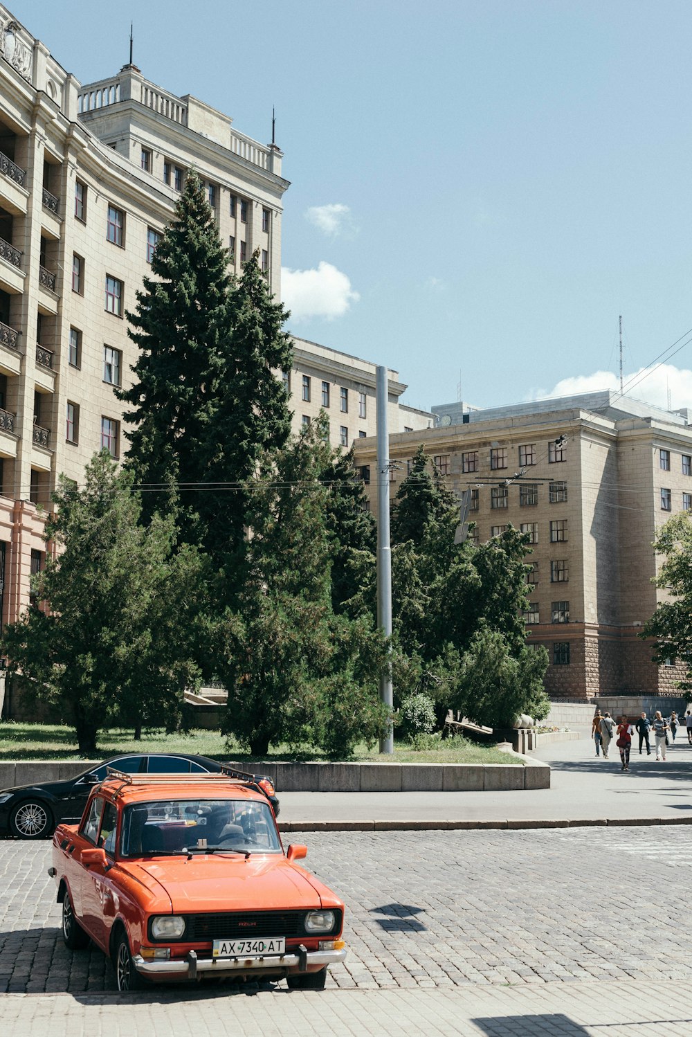 red car on road near green trees and brown concrete building during daytime