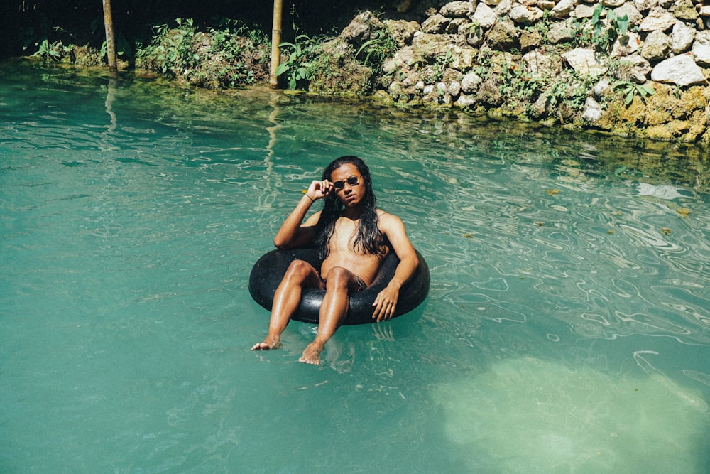 woman in black bikini sitting on rock in water during daytime
