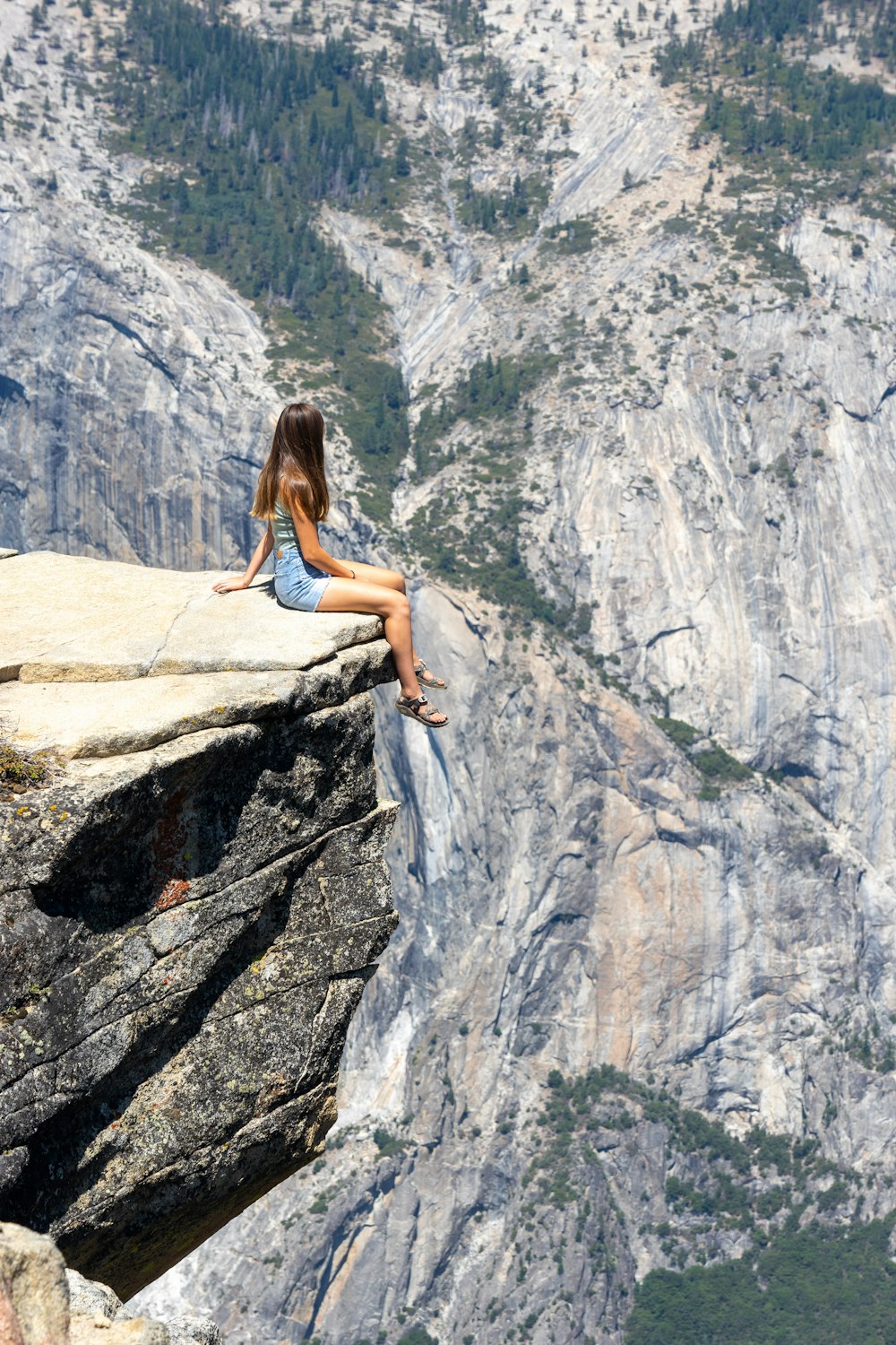 woman in white tank top and blue denim shorts sitting on rock formation during daytime