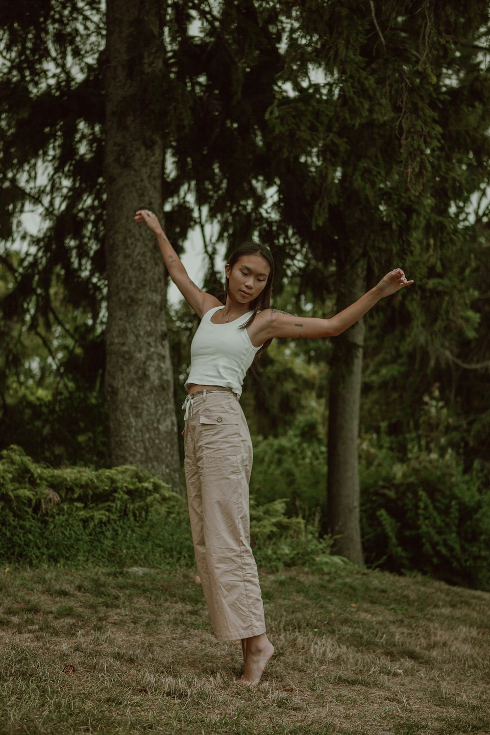 woman in white tank top and beige pants standing on green grass field