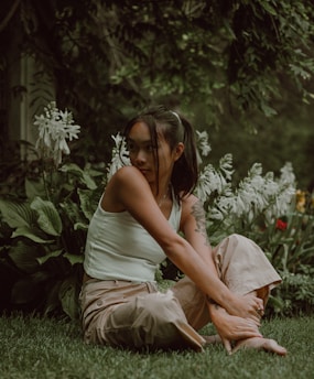 A serene woman sitting cross-legged in a sunlit garden, surrounded by blooming flowers and soft greenery.