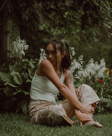A serene woman sitting cross-legged in a sunlit garden, surrounded by blooming flowers and soft greenery.