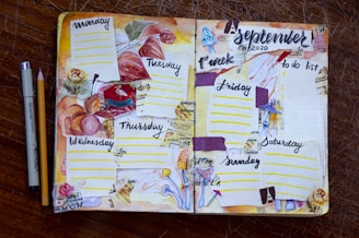 A hand-crafted planner spread for the first week of September 2020, featuring a floral and autumn theme. Each day of the week is sectioned off with colorful decorations, including pressed leaves, floral drawings, and textured paper strips. The layout is lively, with a variety of elements such as dotted lines for daily entries, a 'to do list' on the right page, and artistic embellishments like stamps and watercolor effects. A pen and pencil are placed beside the planner on a wooden surface.