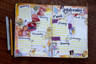 A hand-crafted planner spread for the first week of September 2020, featuring a floral and autumn theme. Each day of the week is sectioned off with colorful decorations, including pressed leaves, floral drawings, and textured paper strips. The layout is lively, with a variety of elements such as dotted lines for daily entries, a 'to do list' on the right page, and artistic embellishments like stamps and watercolor effects. A pen and pencil are placed beside the planner on a wooden surface.
