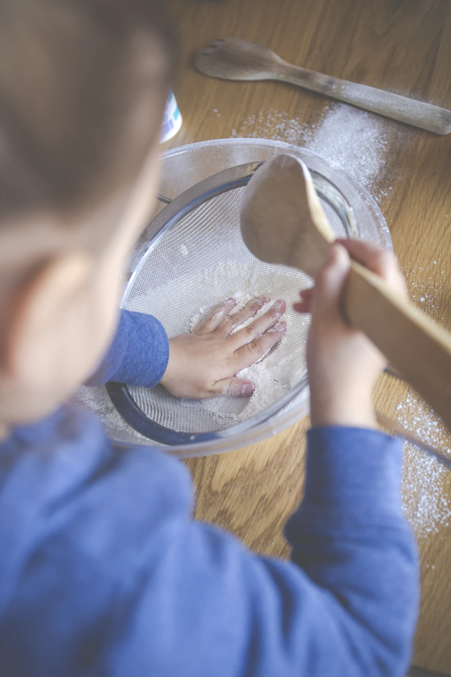 child in blue long sleeve shirt holding brown wooden rolling pin