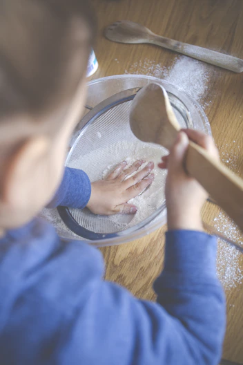 child in blue long sleeve shirt holding brown wooden rolling pin