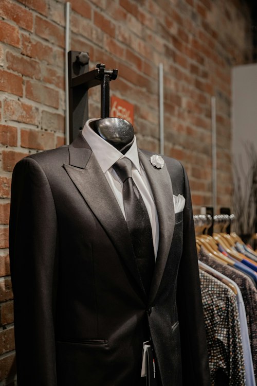 Single suit jacket on a mannequin hung against a brick wall with shirts on a rack
