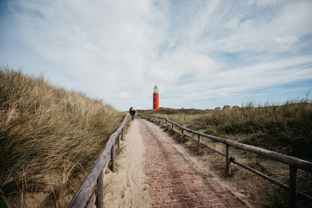 brown wooden pathway between green grass field under white clouds during daytime