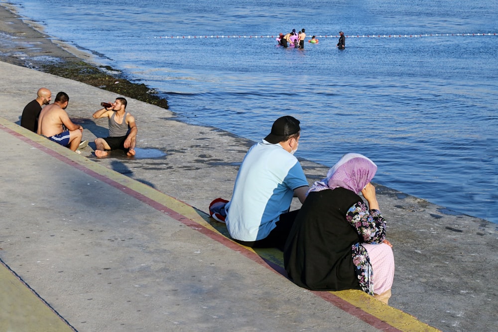 man and woman sitting on concrete dock near body of water during daytime