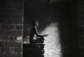 Dark-themed photo showing a person meditating in a minimalist room, symbolizing balance and clarity.