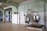 A large industrial kitchen with two massive stainless steel mixing bowls or vats. The room features pale green walls with white tile covering the lower half and a ceiling crisscrossed with exposed beams. Several canned goods and containers are neatly arranged on a shelf above the mixers. The space is well-lit with a lamp hanging from the ceiling.