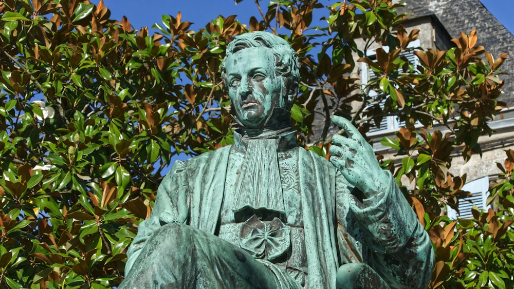 statue of man holding book under blue sky during daytime