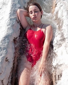 A person in a red swimsuit is relaxing in flowing water, surrounded by white travertine formations, with eyes closed and a serene expression.
