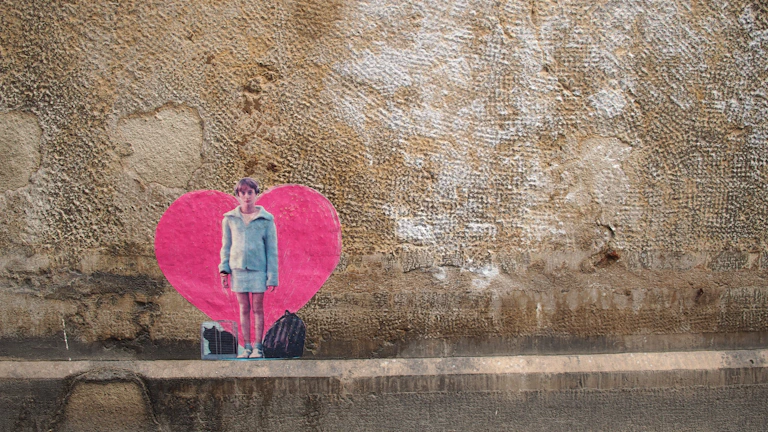 A vibrant Banksy mural of a girl releasing a heart-shaped balloon on a weathered brick wall.