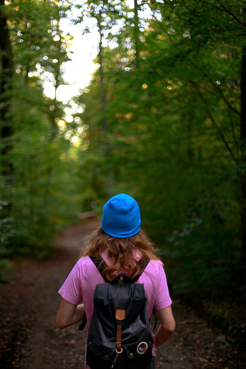 woman in pink long sleeve shirt and blue knit cap standing in forest during daytime