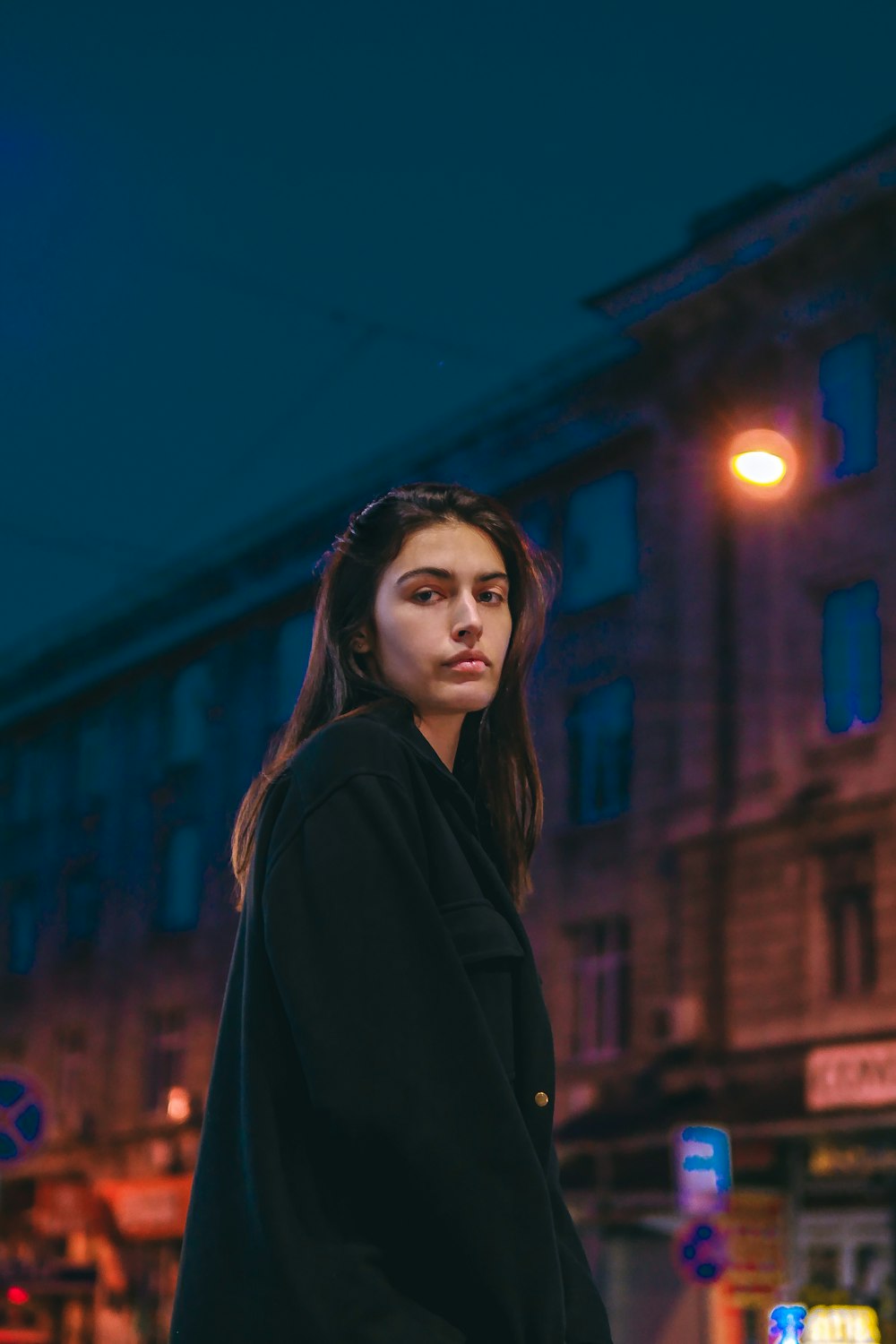 uma mulher em pé em uma esquina da rua à noite