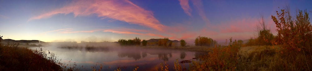 body of water near trees during sunset