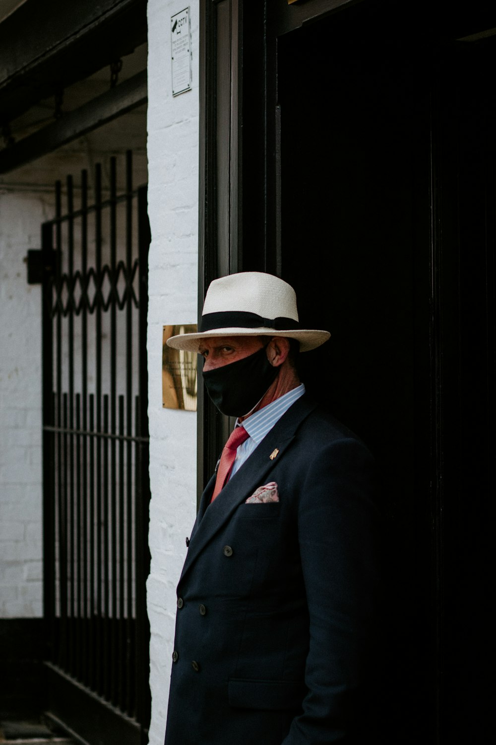 man in black suit wearing brown hat standing near black metal gate during daytime