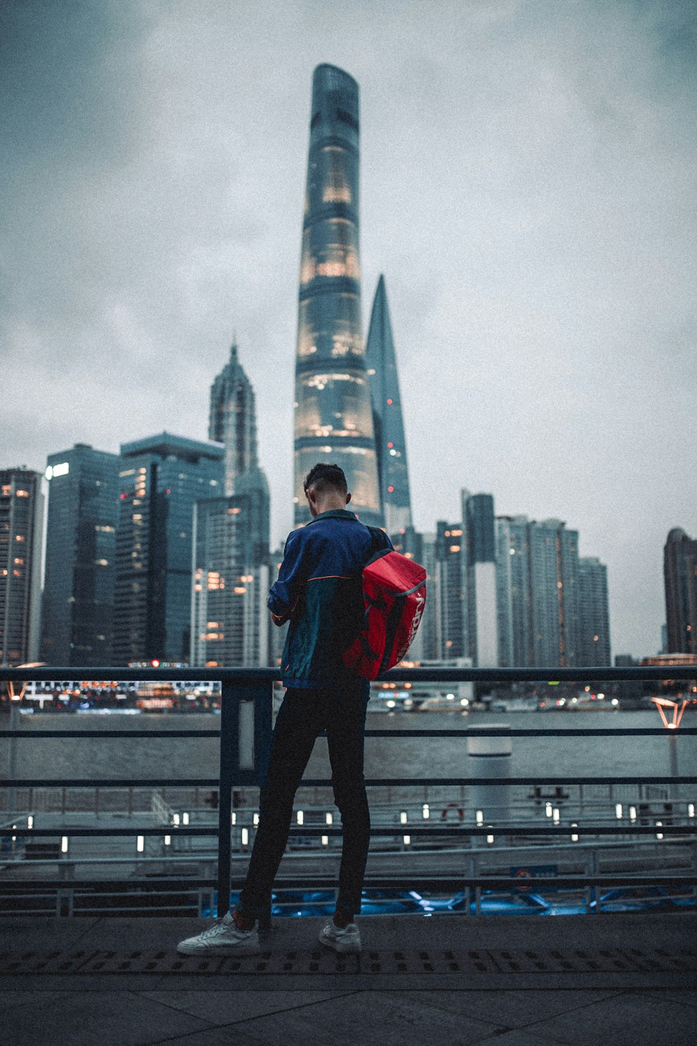 Hombre con sudadera con capucha roja y pantalones negros de pie sobre barandillas de metal negro