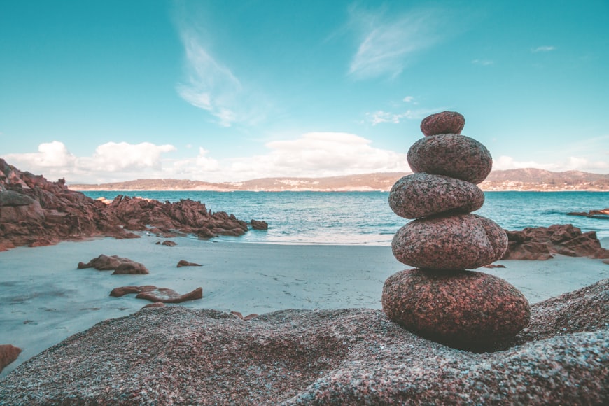 A small pile of rocks is stacked along a calm shoreline. It represents finding balance within and stillness in our mind.
