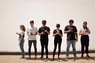 A group of people standing on brown floor each person is looking at and holding a mobile phone.