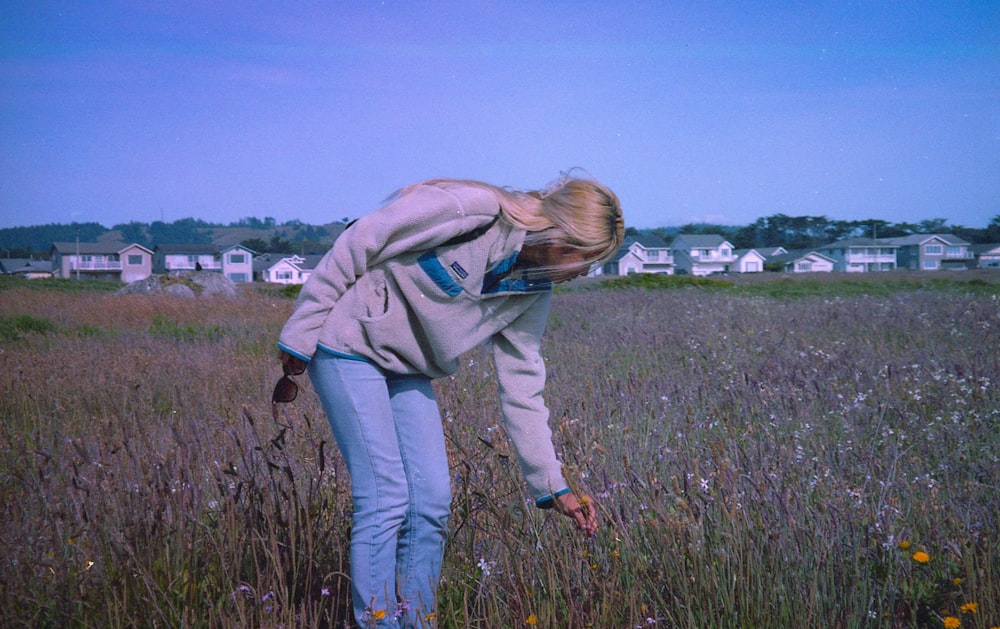 woman in green hoodie and blue denim jeans standing on green grass field during daytime