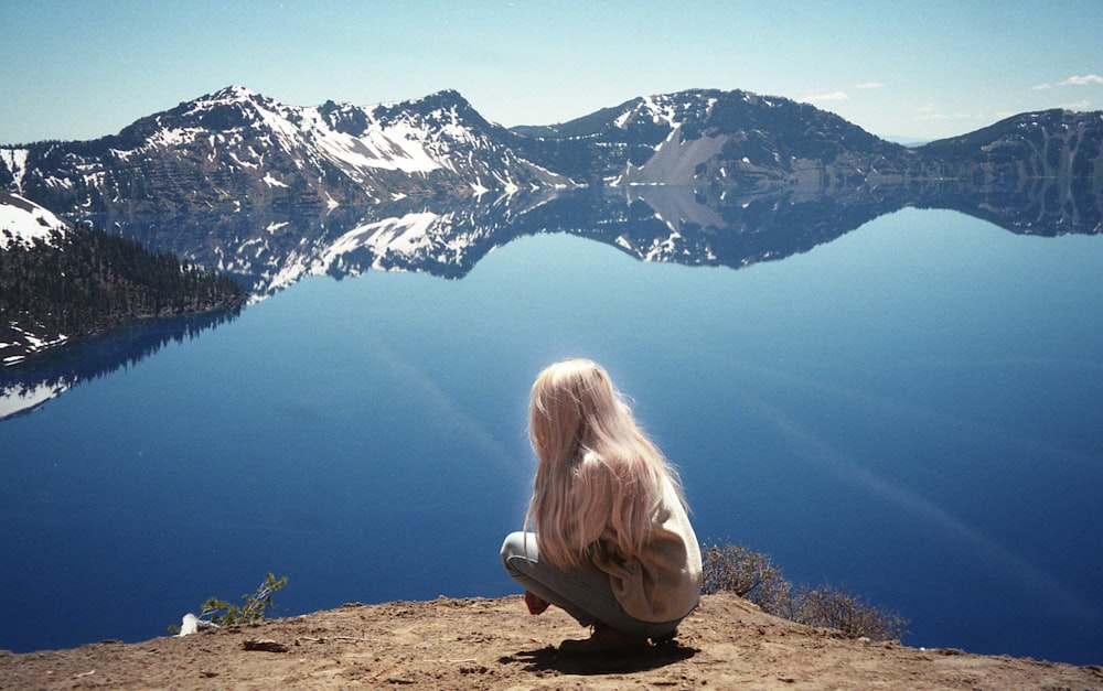 Femme en chemise blanche assise sur un rocher brun regardant la montagne enneigée pendant la journée