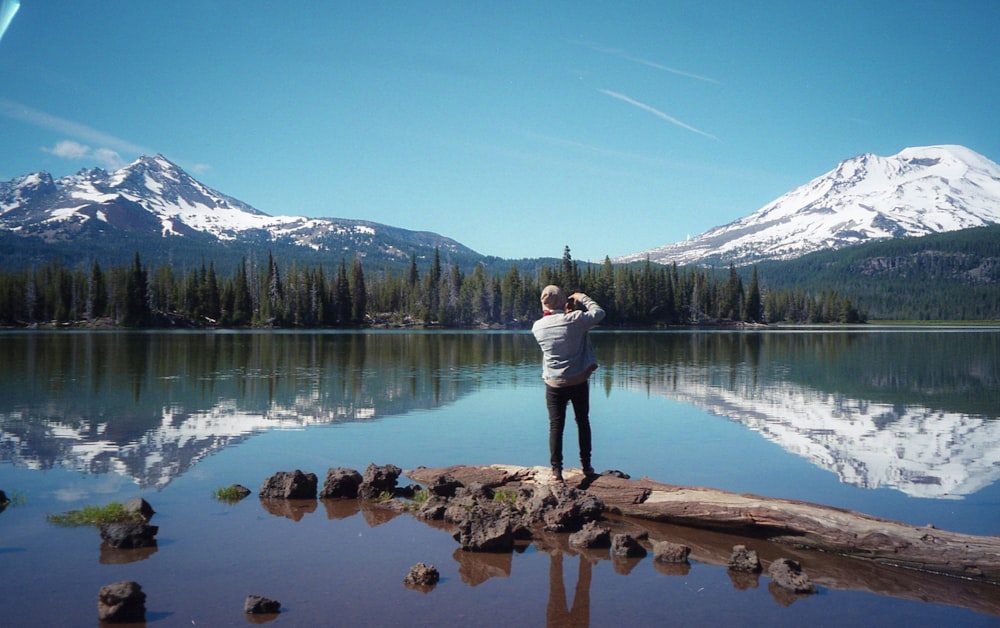 woman in white long sleeve shirt and blue denim jeans standing on brown log near lake