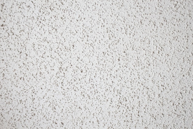 A close-up view of a textured white popcorn ceiling, characterized by its bumpy and uneven surface.