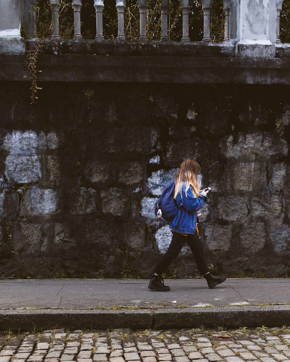 girl in blue jacket and black pants standing on sidewalk during daytime