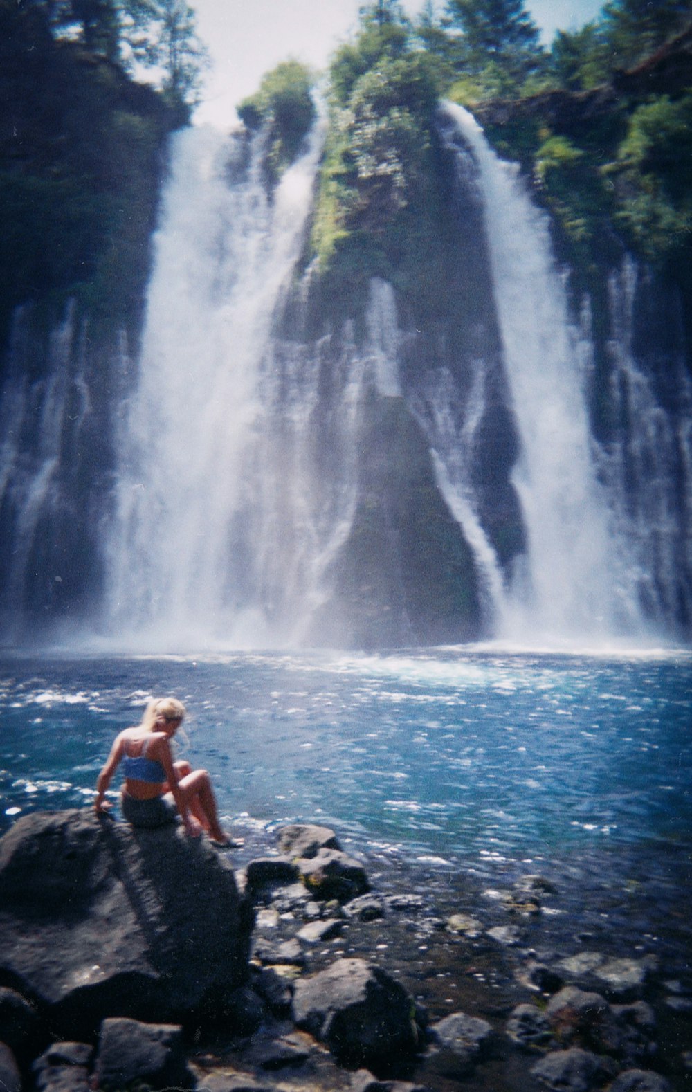woman in black bikini sitting on rock near waterfalls during daytime