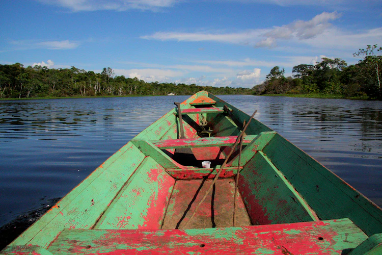 Wooden canoe on calm Amazon river water, rainforest behind