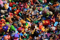 A chaotic assortment of colorful toys piled together, including action figures, plush animals, vehicles, and various shapes and characters. The variety of toys suggests a playful and imaginative setting.
