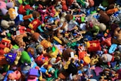 A chaotic assortment of colorful toys piled together, including action figures, plush animals, vehicles, and various shapes and characters. The variety of toys suggests a playful and imaginative setting.