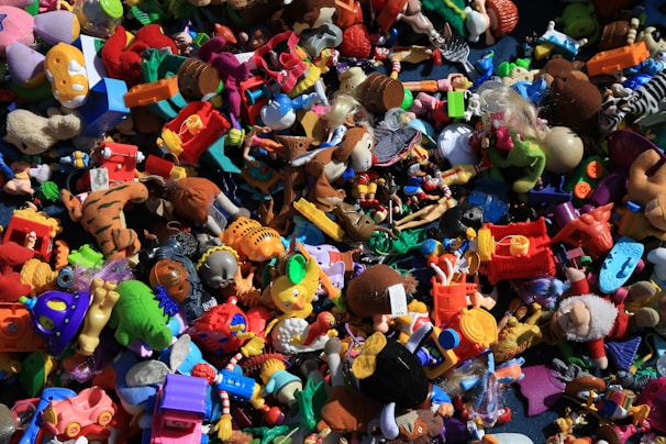 A chaotic assortment of colorful toys piled together, including action figures, plush animals, vehicles, and various shapes and characters. The variety of toys suggests a playful and imaginative setting.