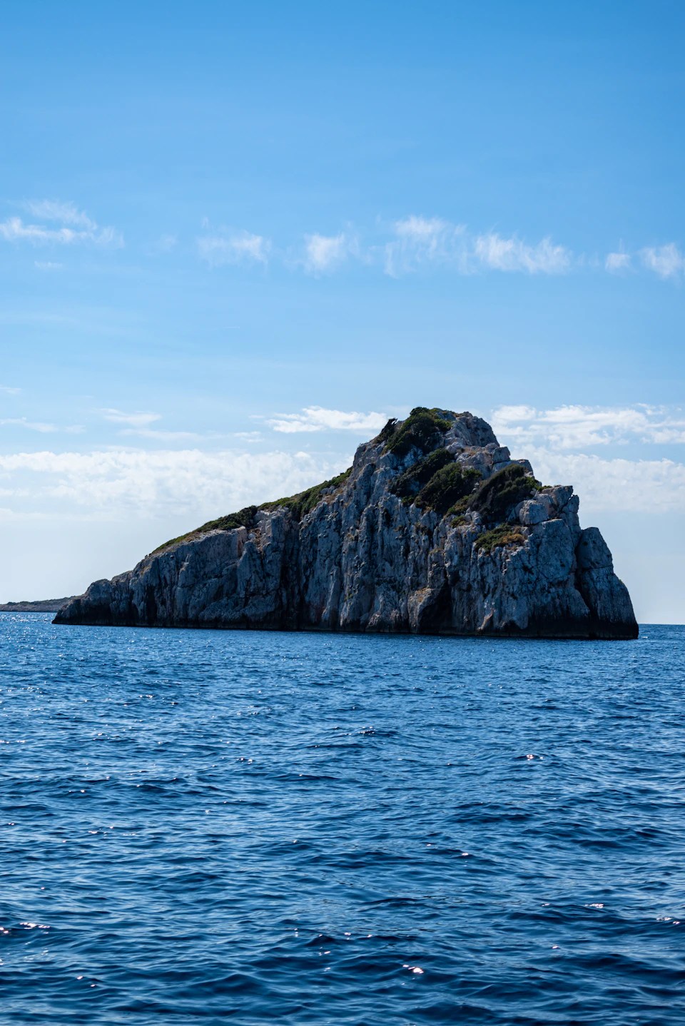 Serene island scene with rocky cliff face and clear blue sky in the distance