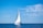A sailing boat gliding on calm blue sea under a clear sky.