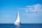 A sailing boat gliding on calm blue sea under a clear sky.