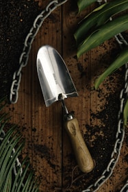 A sturdy garden trowel with a wooden handle placed on rich soil beside blooming flowers.
