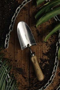 A sturdy garden trowel with a comfortable grip lying on fresh soil with green plants around.