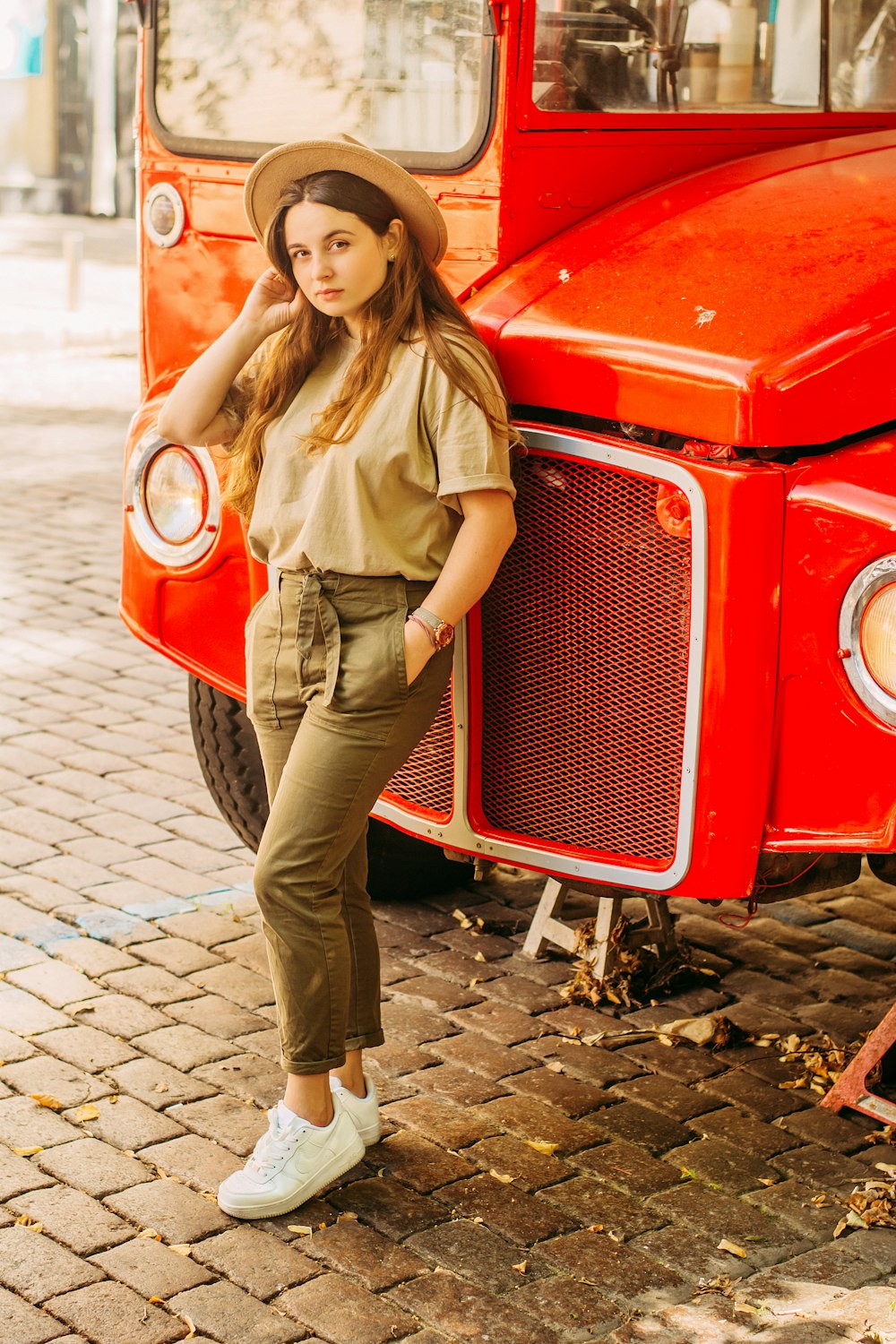 woman in brown button up shirt and brown pants leaning on red car