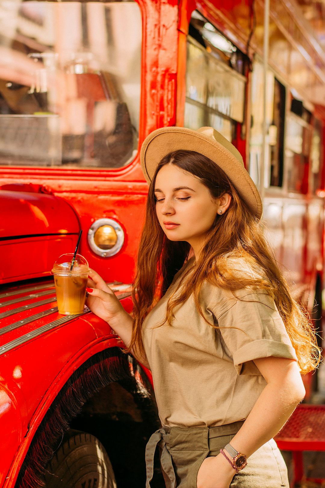 woman in brown coat holding cup standing beside red car during daytime