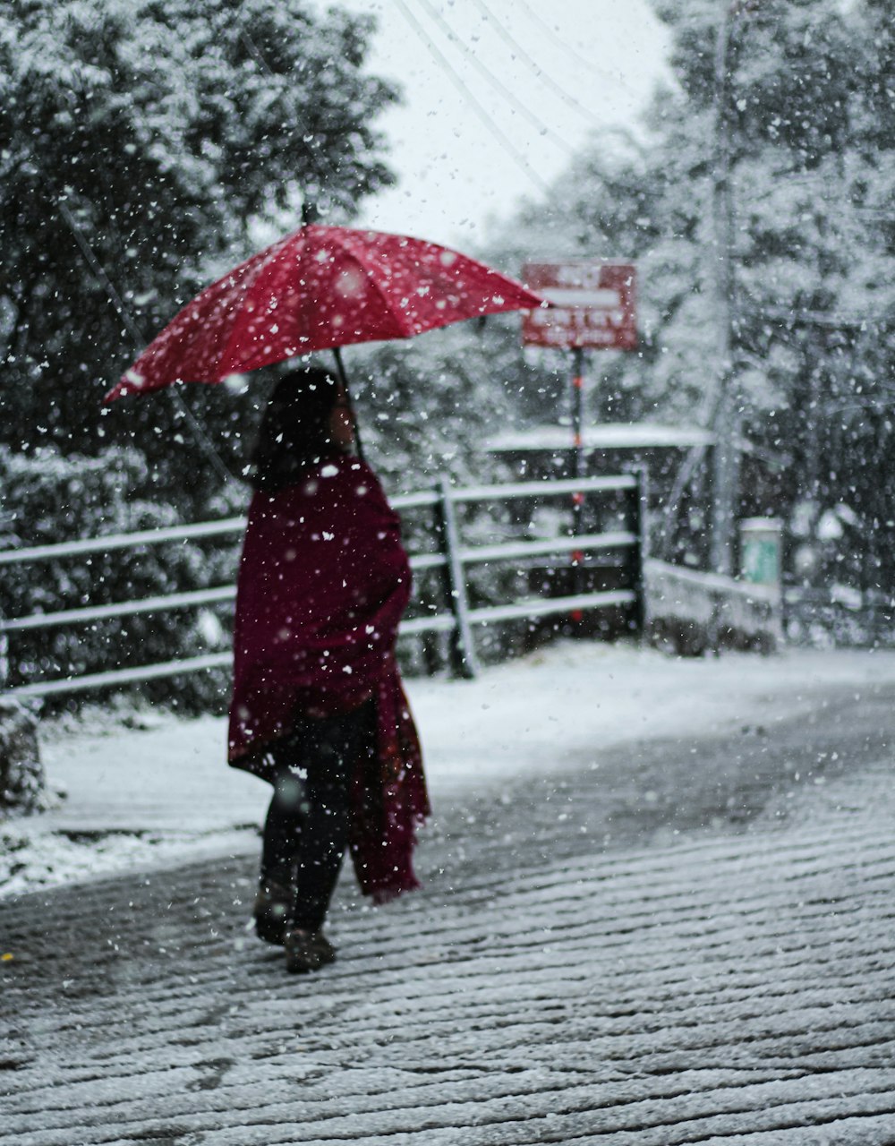 昼間、雪に覆われた地面に立つ傘を持つ赤いコートの女性