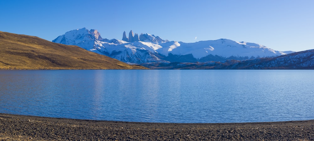 lago azul perto de montanhas marrons e brancas sob o céu azul durante o dia