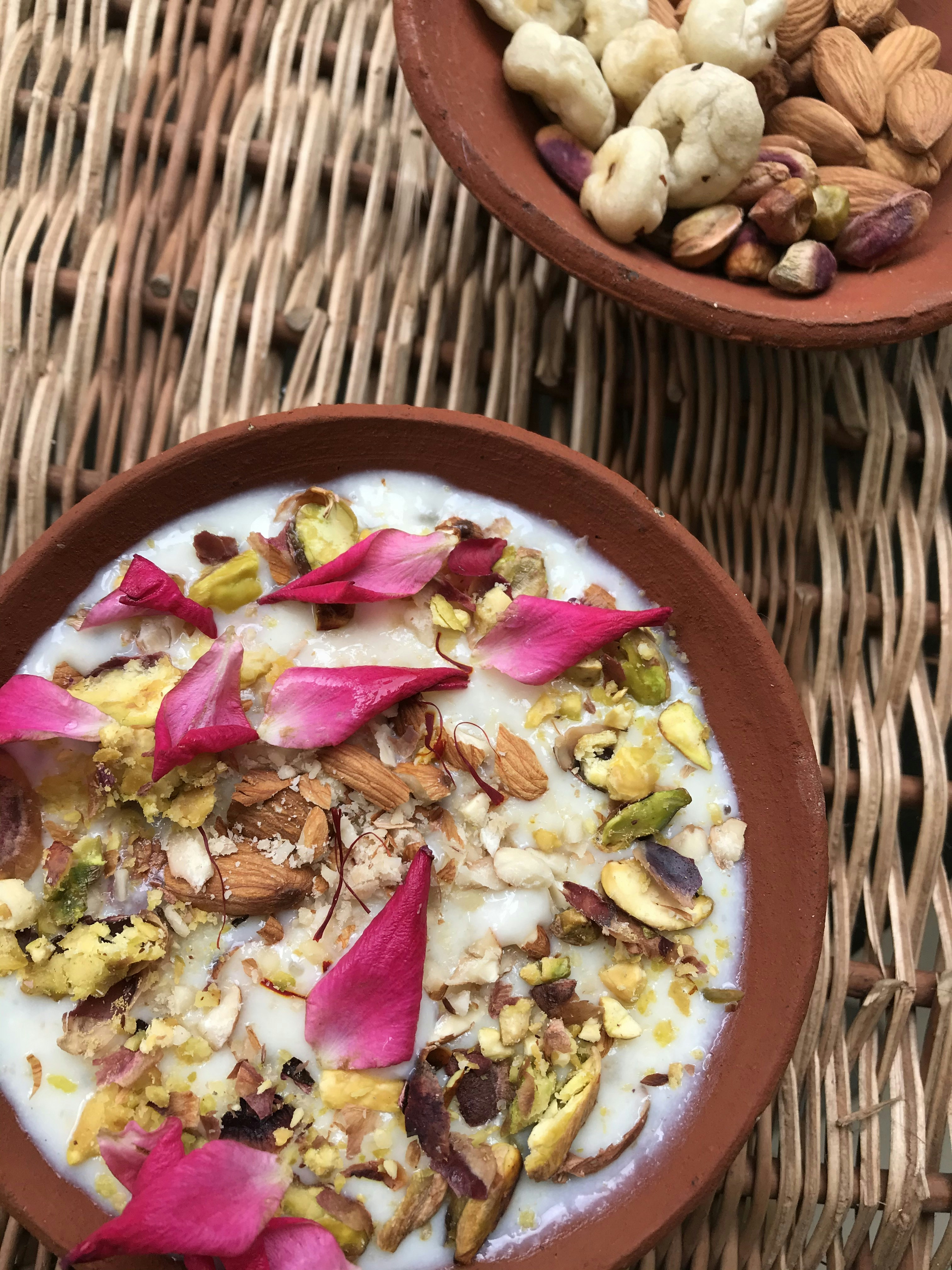 Malaiyo winter sweet dessert in clay bowl, airy foam topped with saffron and rose petals, warm natural light