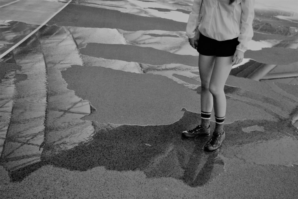 灰色のコンクリートの道を歩く白い長袖シャツと黒いスカートの女性