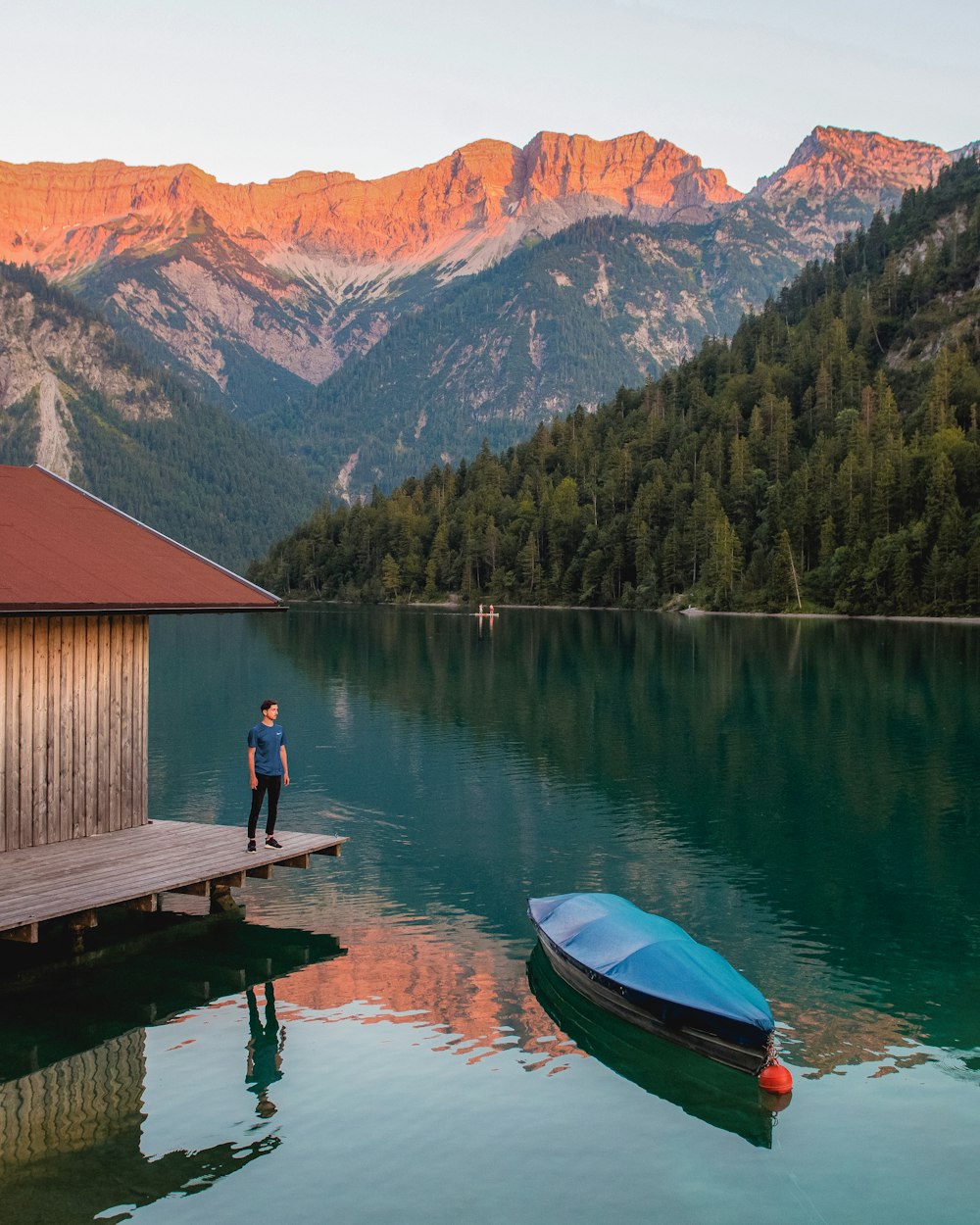 person in green jacket sitting on brown wooden dock during daytime