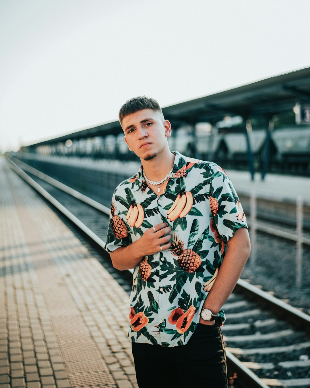 man in white red and black floral button up t-shirt standing on train rail during